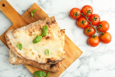 Photo of Halves of tasty calzone, basil, sauce and tomato on white marble table, flat lay