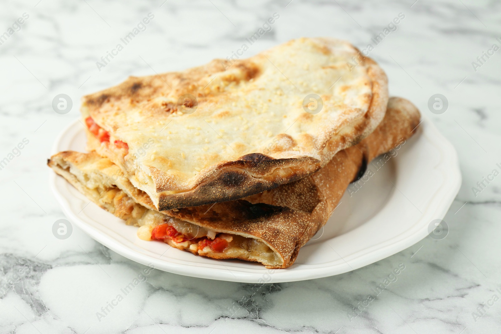 Photo of Halves of tasty calzone with meat, cheese and tomato on white marble table, closeup