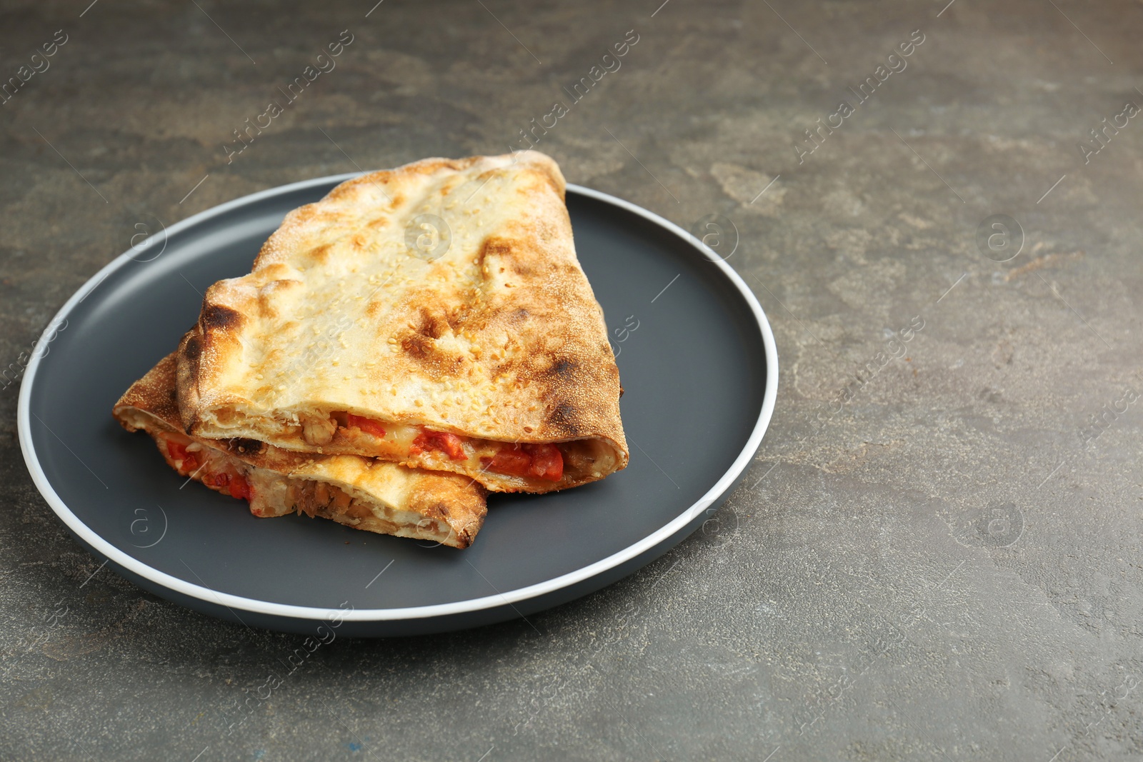 Photo of Halves of tasty calzone with meat, cheese and tomato on grey textured table, closeup. Space for text