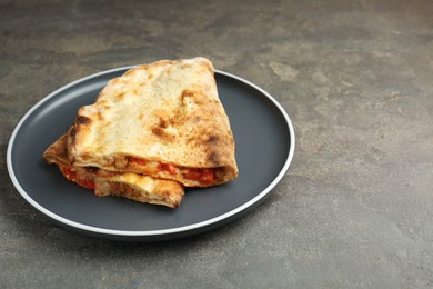 Photo of Halves of tasty calzone with meat, cheese and tomato on grey textured table, closeup. Space for text