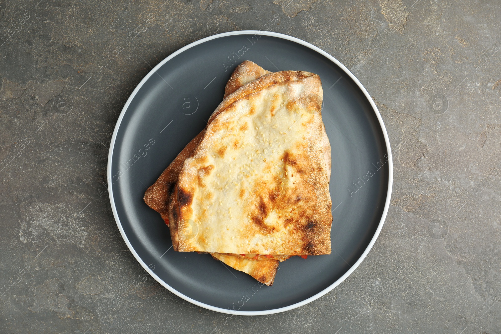 Photo of Halves of tasty calzone on grey textured table, top view