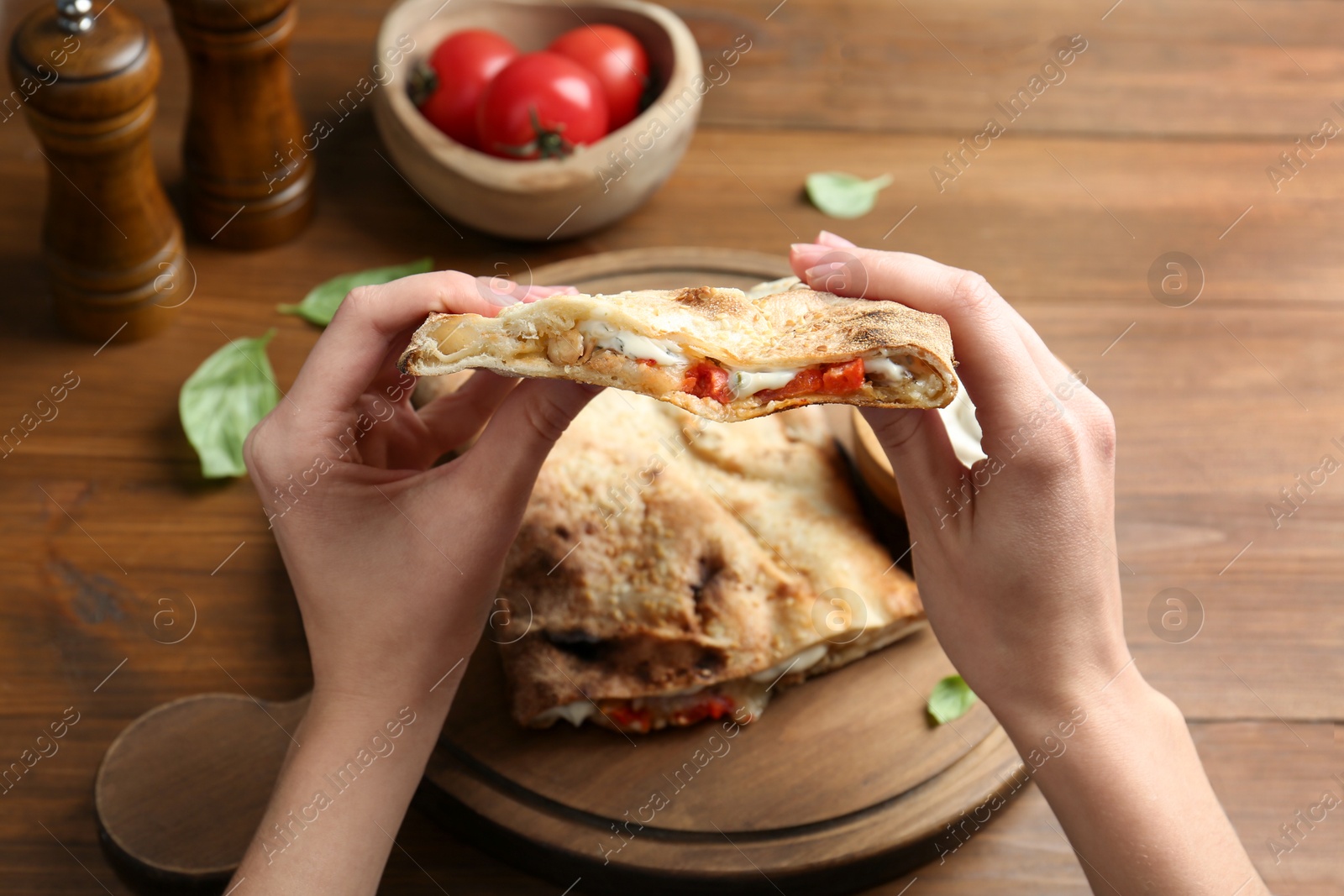 Photo of Woman eating tasty calzone with meat, cheese and tomato at wooden table, closeup