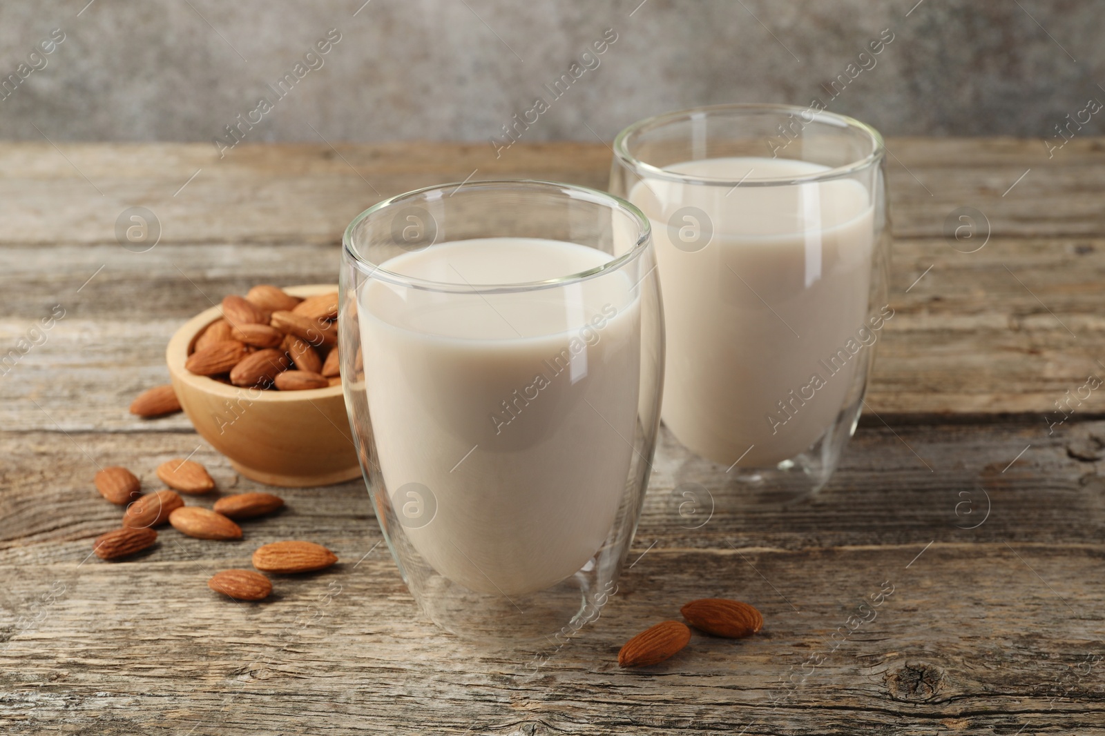 Photo of Fresh nut milk in glasses and almonds on wooden table, closeup