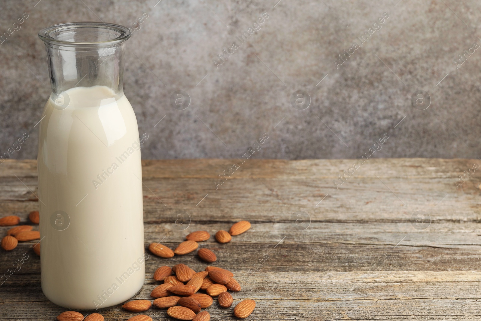 Photo of Fresh nut milk in jug and almonds on wooden table. Space for text