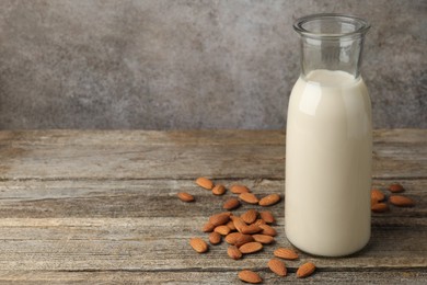 Photo of Fresh nut milk in jug and almonds on wooden table. Space for text