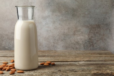 Photo of Fresh nut milk in jug and almonds on wooden table. Space for text