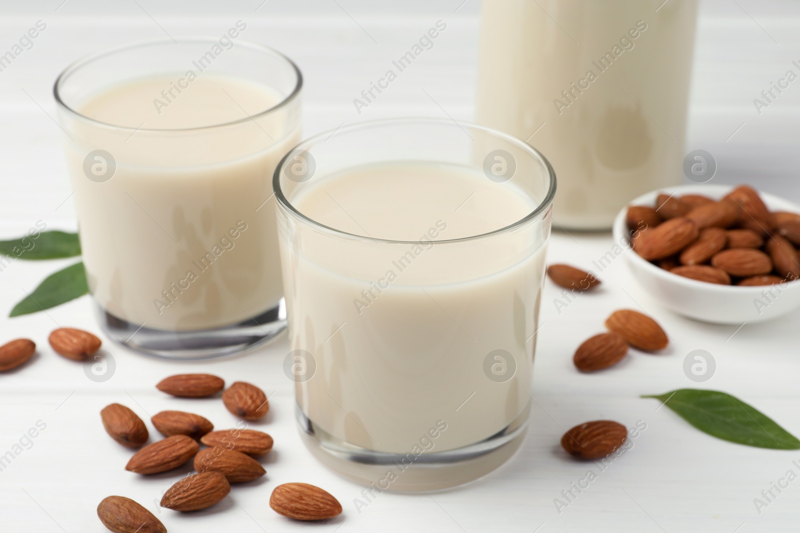 Photo of Fresh nut milk, green leaves and almonds on white wooden table, closeup