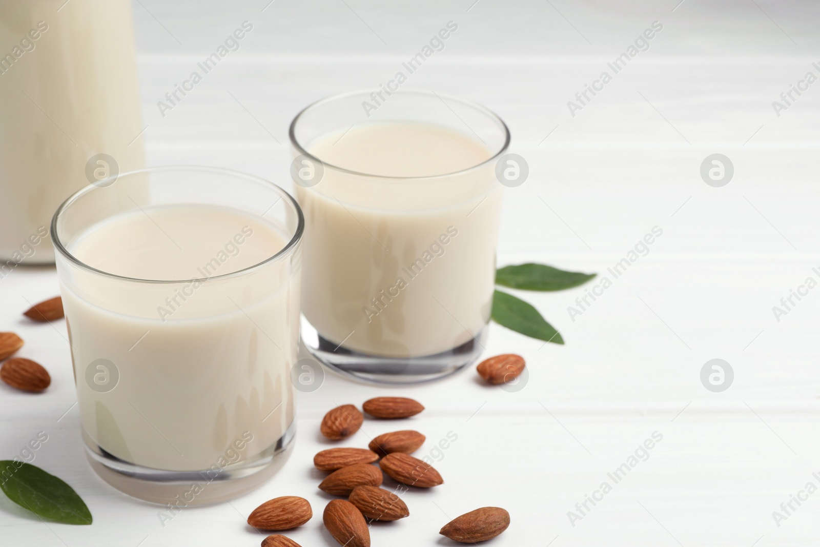 Photo of Fresh nut milk, green leaves and almonds on white wooden table, closeup. Space for text