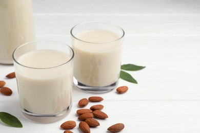 Photo of Fresh nut milk, green leaves and almonds on white wooden table, closeup. Space for text