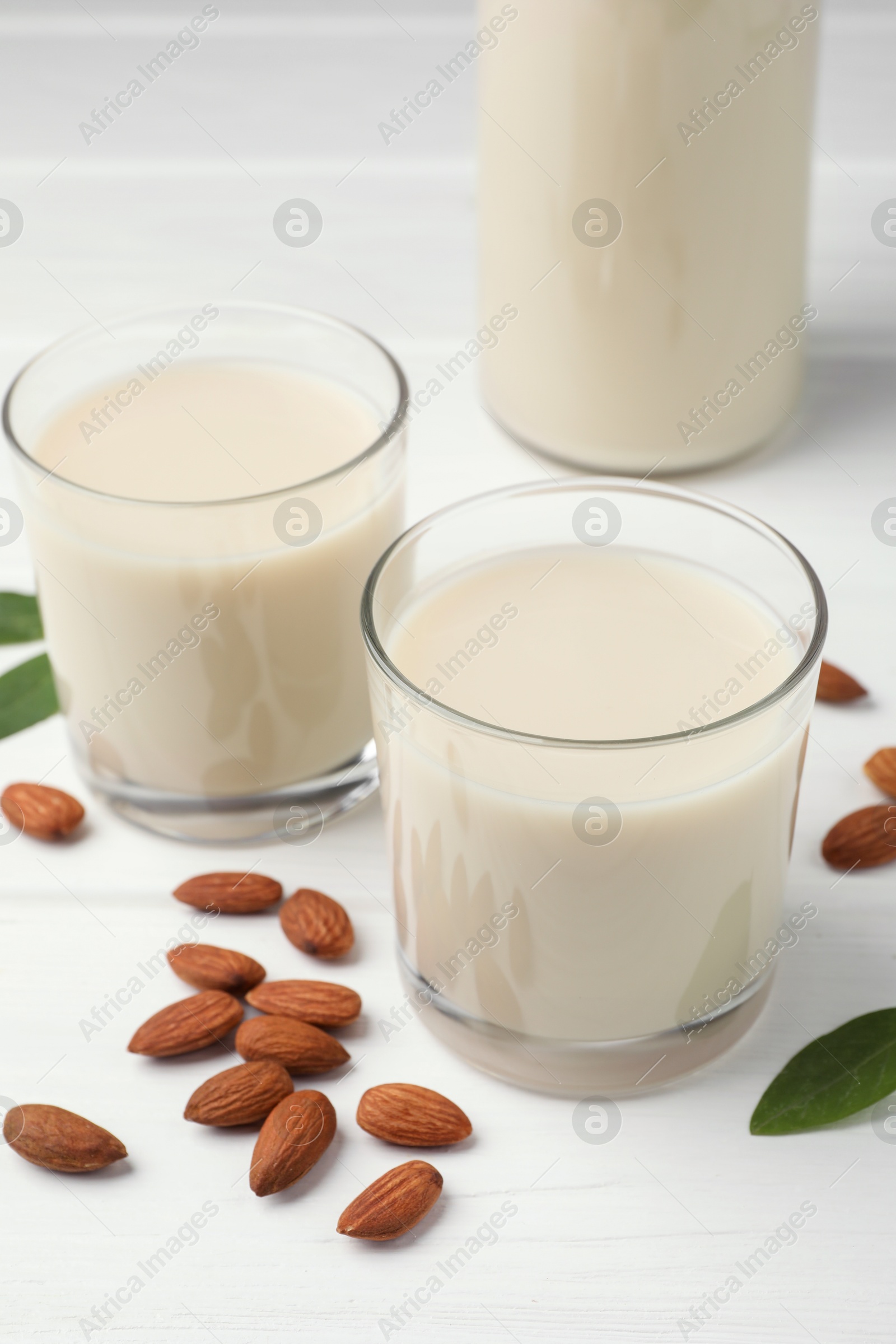 Photo of Fresh nut milk, green leaves and almonds on white wooden table, closeup