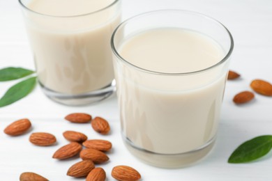 Photo of Fresh nut milk in glasses, green leaves and almonds on white wooden table, closeup