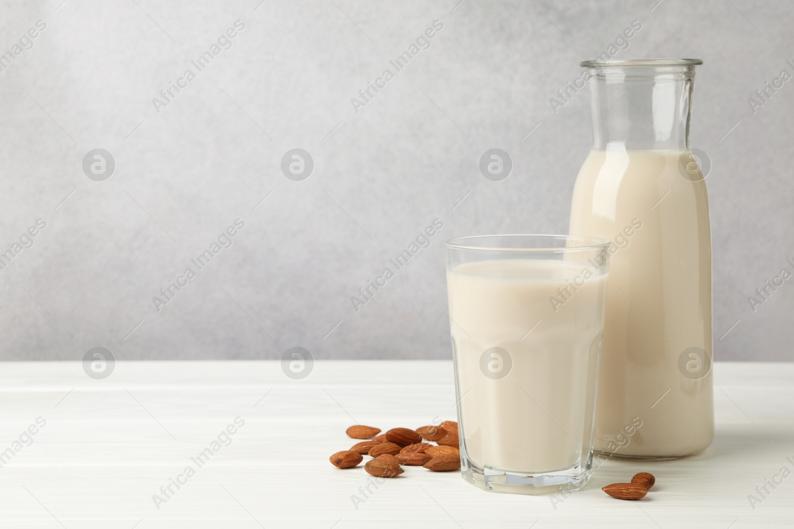 Photo of Fresh nut milk and almonds on white wooden table. Space for text