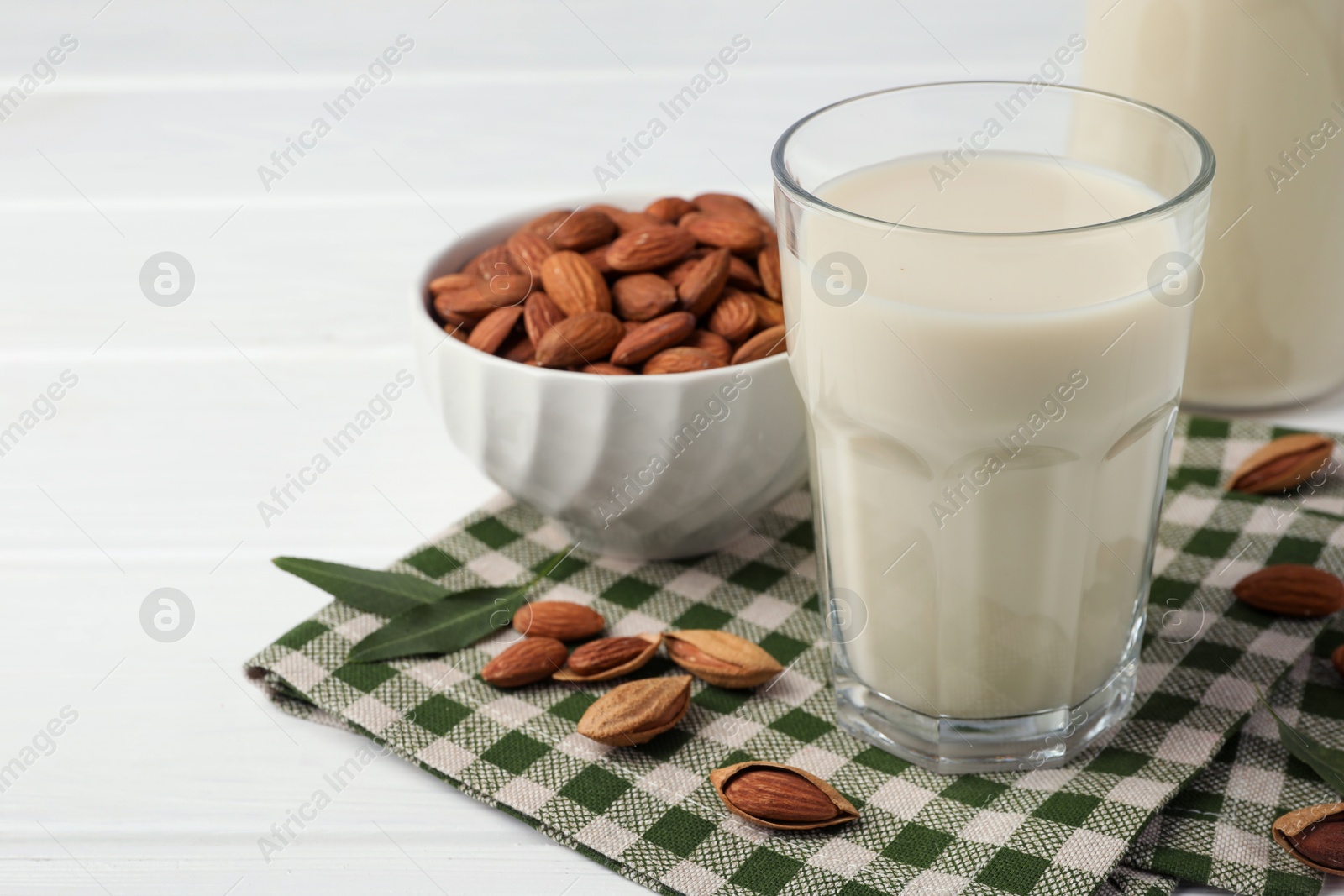 Photo of Fresh nut milk and almonds on white table, closeup. Space for text