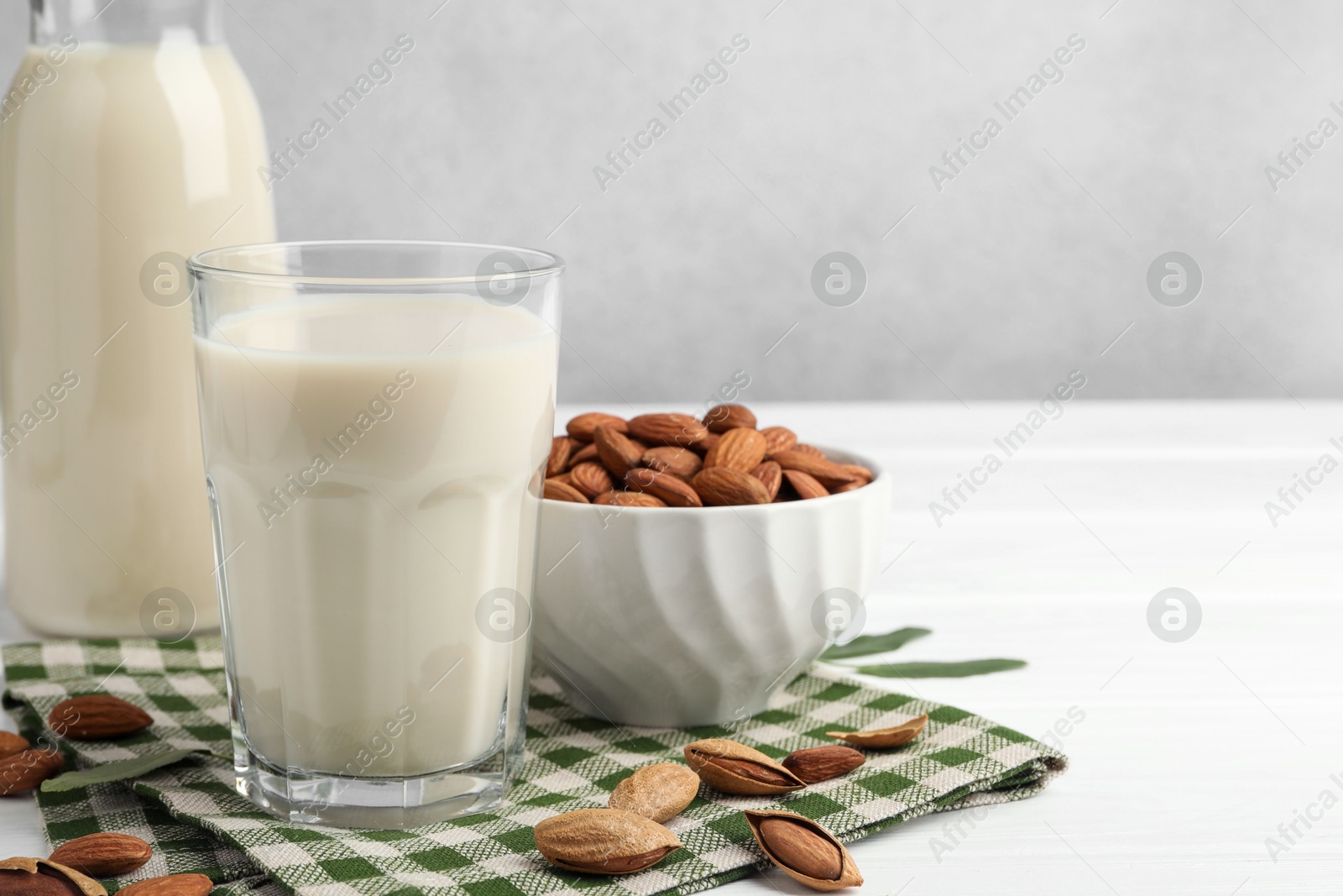 Photo of Fresh nut milk and almonds on white wooden table, closeup. Space for text