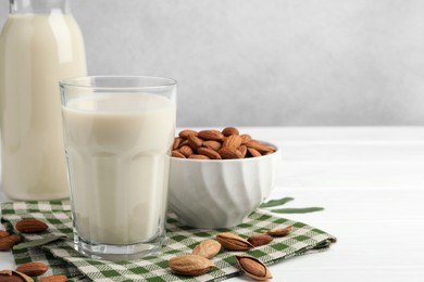 Fresh nut milk and almonds on white wooden table, closeup. Space for text