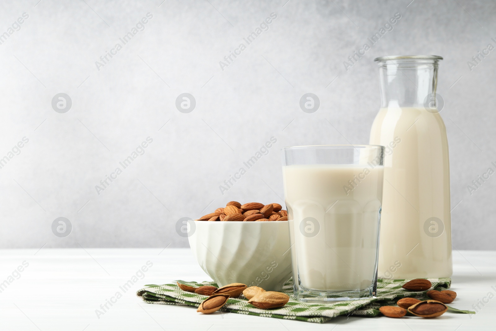 Photo of Fresh nut milk and almonds on white wooden table, space for text