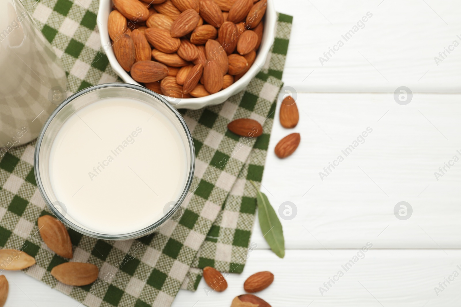 Photo of Fresh nut milk and almonds on white wooden table, flat lay. Space for text