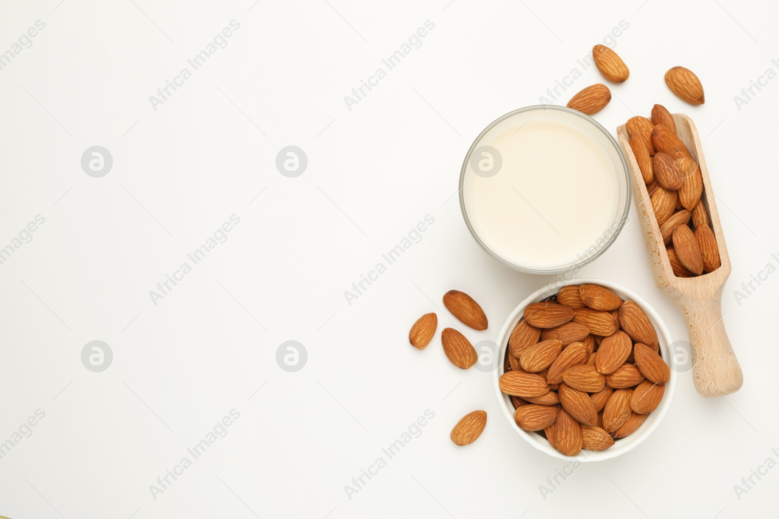 Photo of Fresh nut milk in glass and almonds on white table, flat lay. Space for text