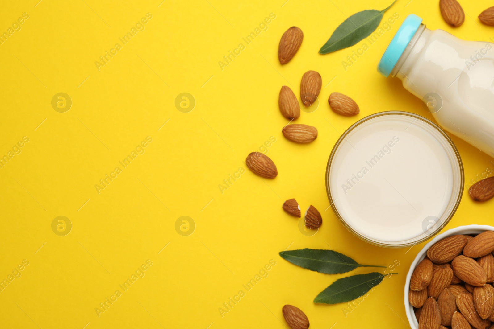 Photo of Fresh nut milk, almonds and green leaves on yellow background, flat lay. Space for text