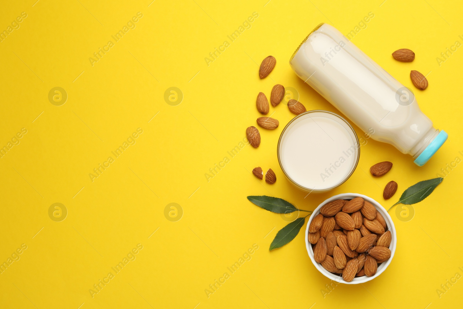 Photo of Fresh nut milk, almonds and green leaves on yellow background, flat lay. Space for text