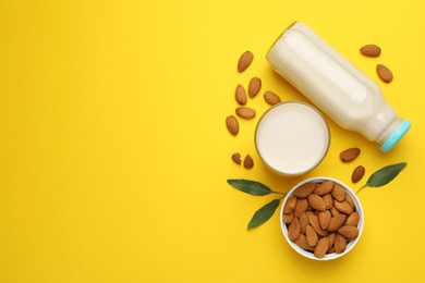 Fresh nut milk, almonds and green leaves on yellow background, flat lay. Space for text