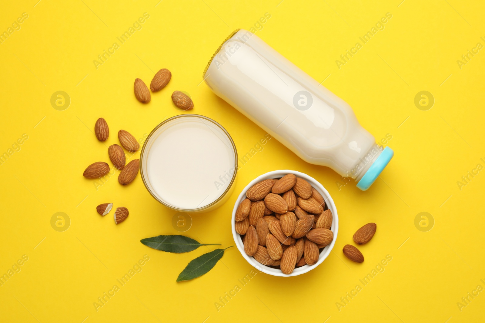 Photo of Fresh nut milk, almonds and green leaves on yellow background, flat lay