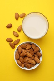 Photo of Fresh nut milk in glass and almonds on yellow background, flat lay