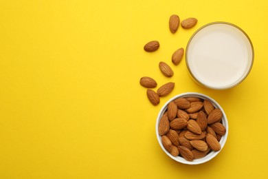 Fresh nut milk in glass and almonds on yellow background, flat lay. Space for text