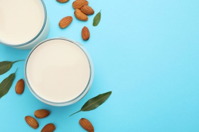 Fresh nut milk in glasses, almonds and green leaves on light blue background, flat lay. Space for text