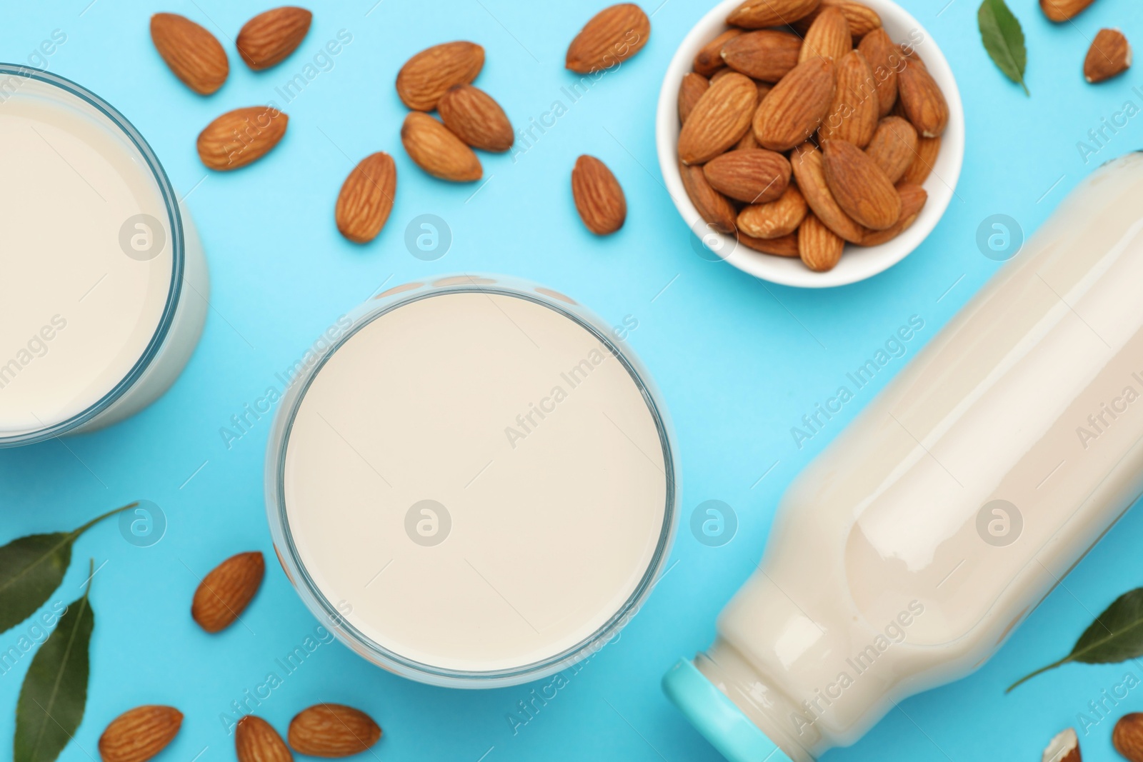 Photo of Fresh nut milk, almonds and green leaves on light blue background, flat lay