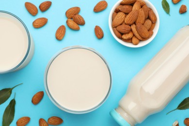 Fresh nut milk, almonds and green leaves on light blue background, flat lay