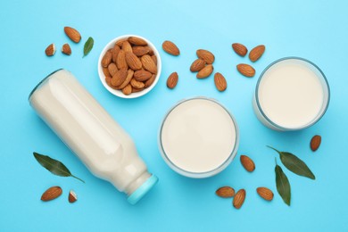 Photo of Fresh nut milk, almonds and green leaves on light blue background, flat lay