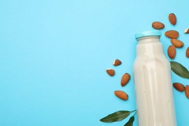 Fresh nut milk in glass bottle, almonds and green leaves on light blue background, top view. Space for text