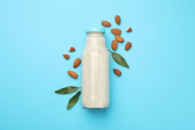 Fresh nut milk in glass bottle, almonds and green leaves on light blue background, top view