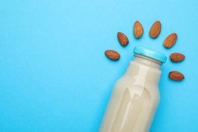 Fresh nut milk in glass bottle and almonds on light blue background, top view. Space for text