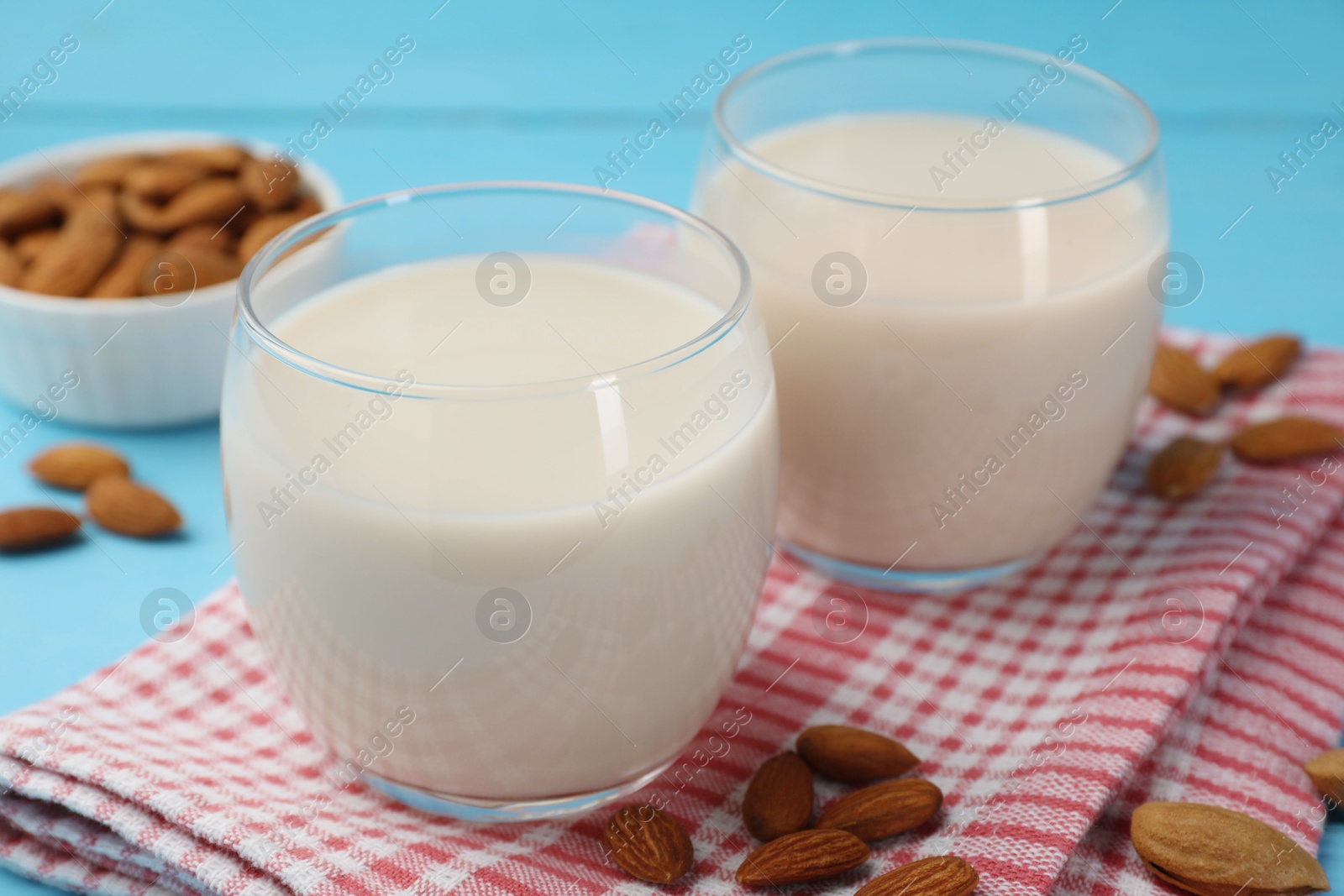 Photo of Fresh nut milk in glasses and almonds on light blue table, closeup