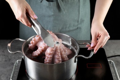 Photo of Woman taking boiled octopus from pan on stove, closeup