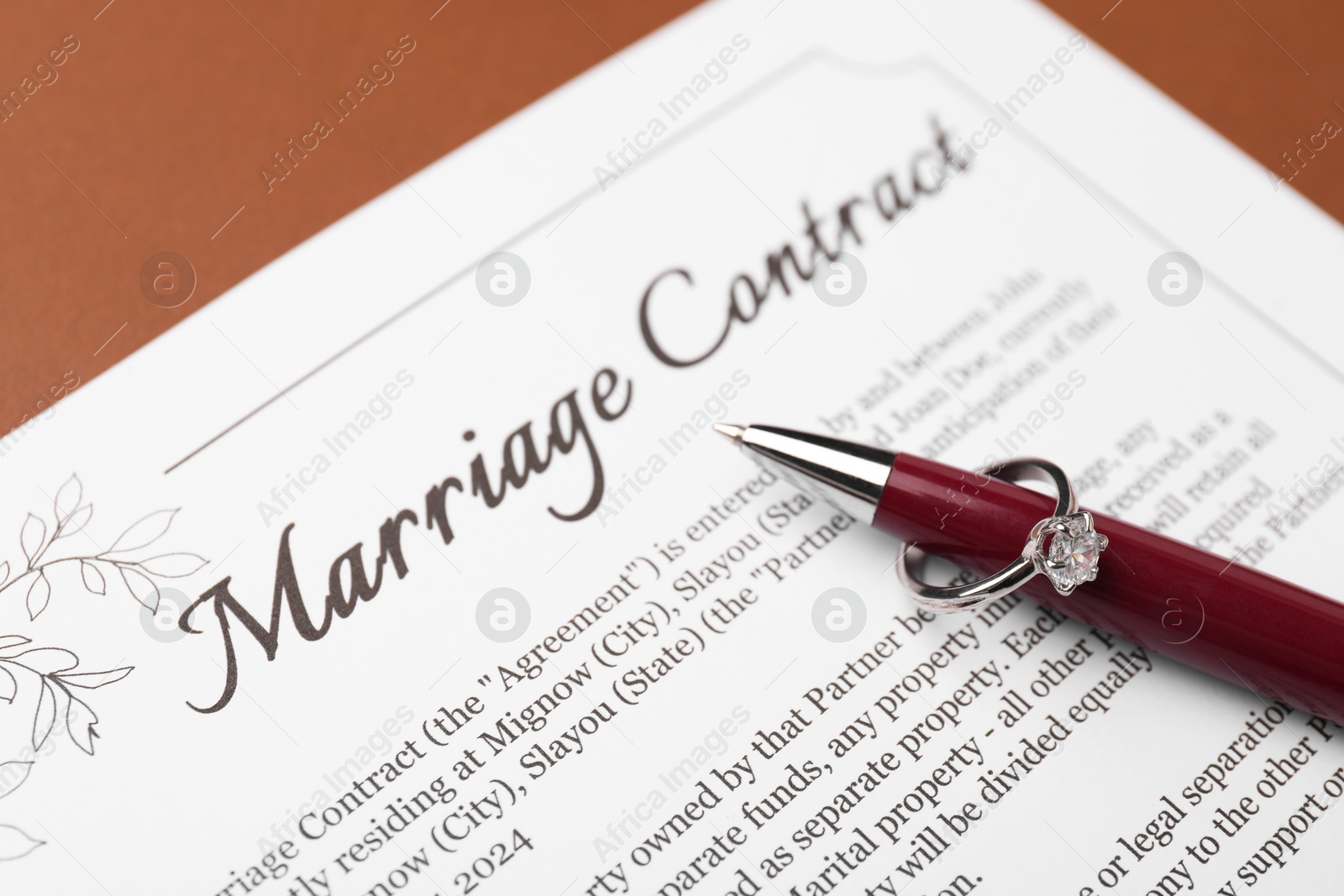 Photo of Marriage contract, pen and ring on brown background, closeup