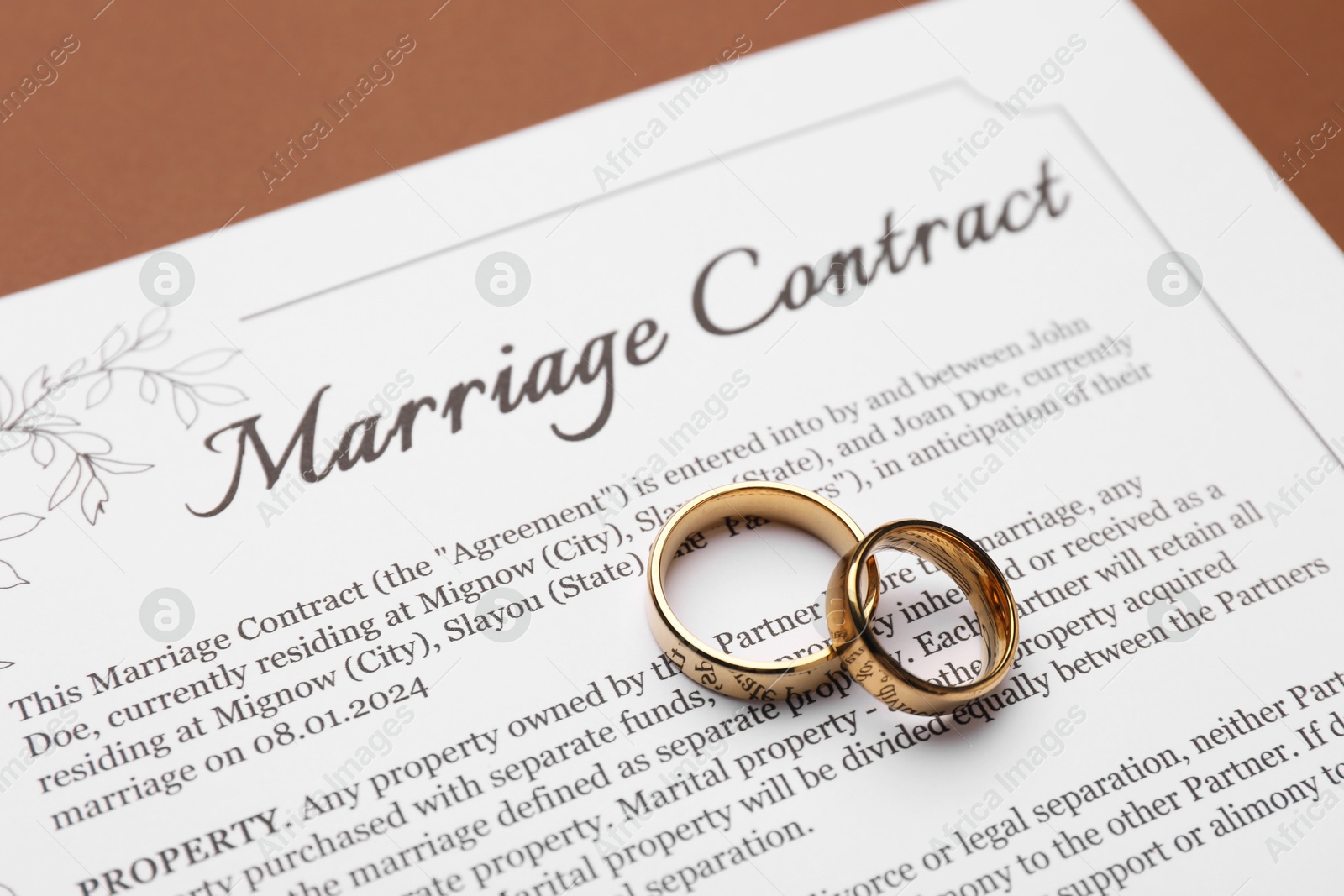 Photo of Marriage contract and golden rings on brown background, closeup