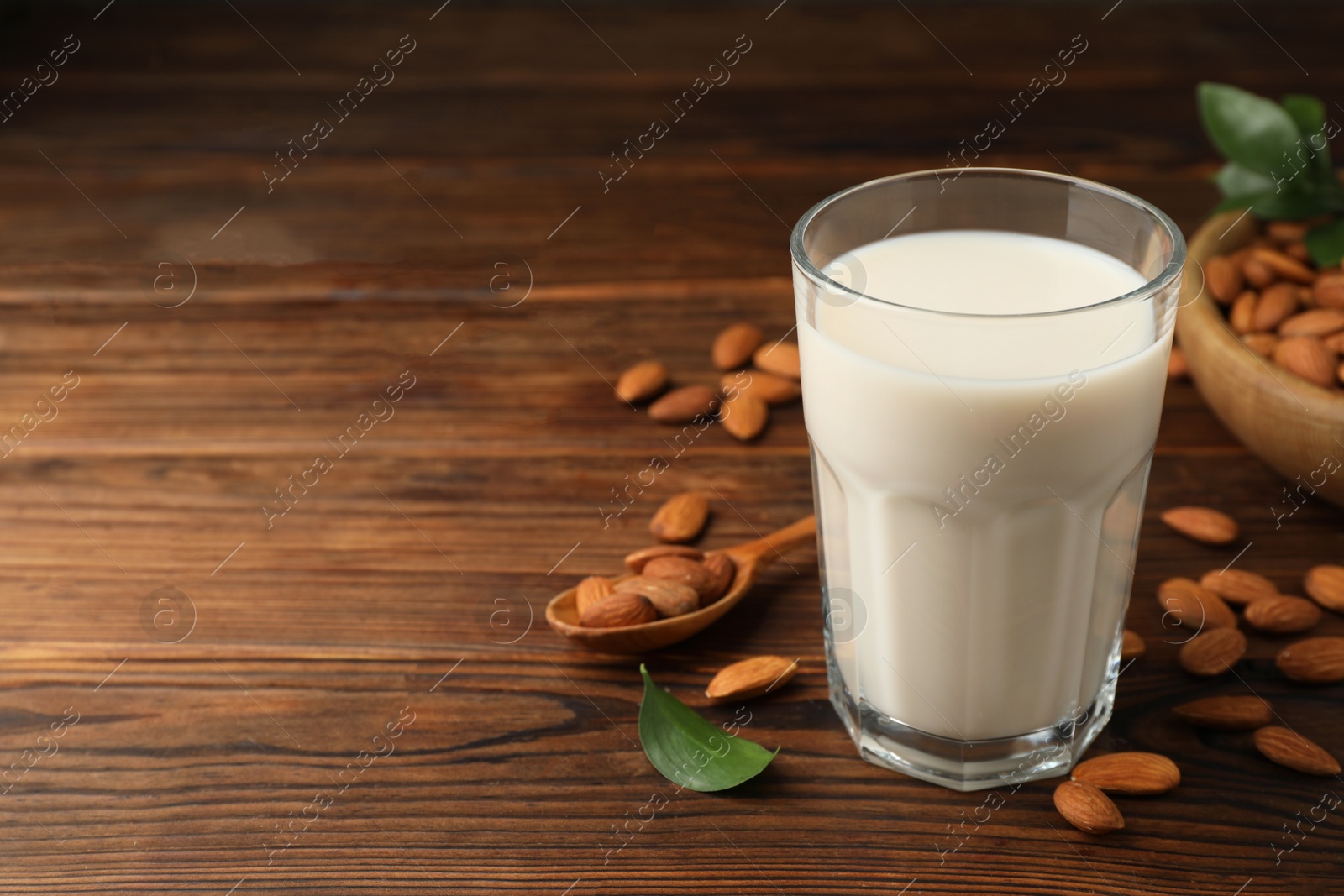 Photo of Fresh almond milk in glass and nuts on wooden table, space for text