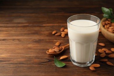 Fresh almond milk in glass and nuts on wooden table, space for text