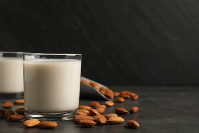 Fresh almond milk in glasses and nuts on dark grey table, space for text