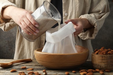 Photo of Making almond milk. Woman pouring nut mixture into cheesecloth at wooden table, closeup