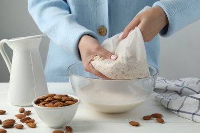 Woman making almond milk at white wooden table, closeup