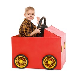 Little boy waving while driving car made of cardboard on white background