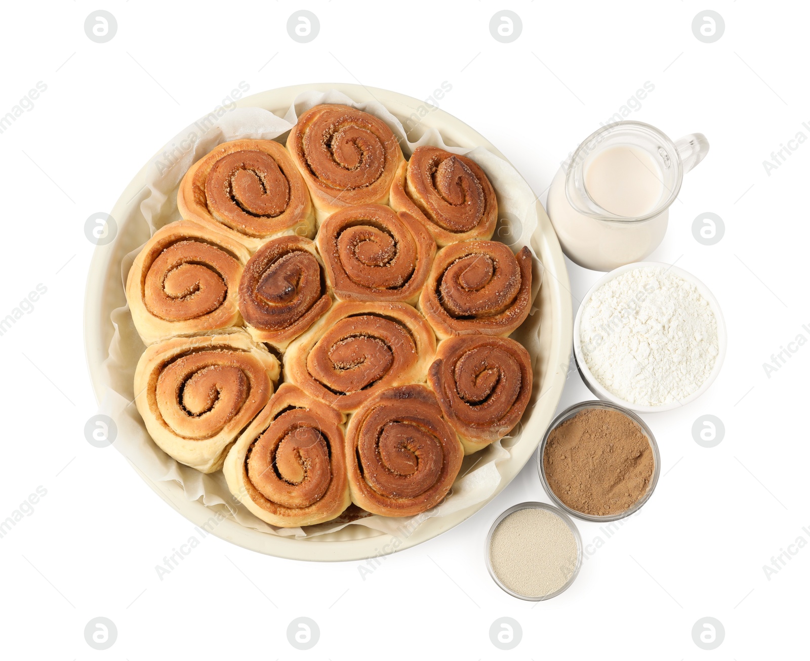 Photo of Freshly baked cinnamon rolls in baking dish and ingredients isolated on white, top view