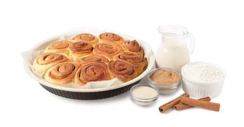 Photo of Freshly baked cinnamon rolls in baking dish and ingredients isolated on white