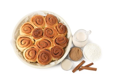 Photo of Freshly baked cinnamon rolls in baking dish and ingredients isolated on white, top view