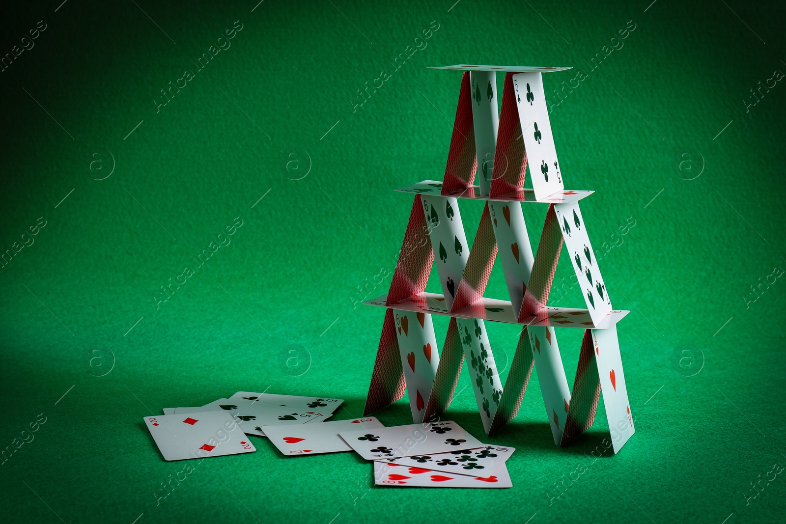 Photo of House of playing cards on green background. Space for text