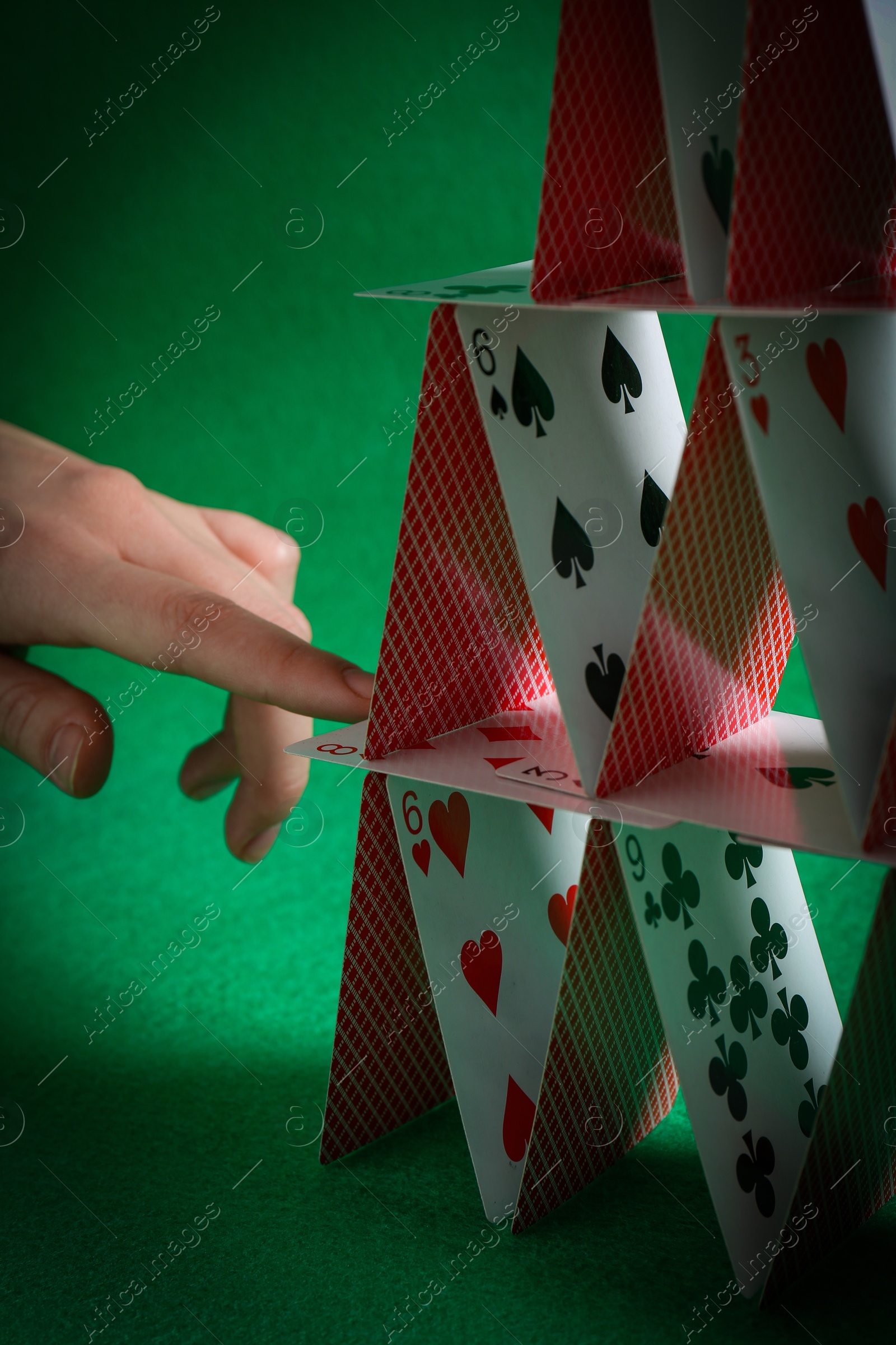 Photo of Woman destroying house of playing cards on green background, closeup